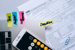Bureau à plat montrant des documents fiscaux, une application de calculatrice sur smartphone, des notes autocollantes et des trombones.