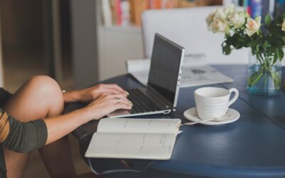 Une personne tape sur un clavier d'ordinateur portable à côté d'un carnet et d'une tasse de café blanche