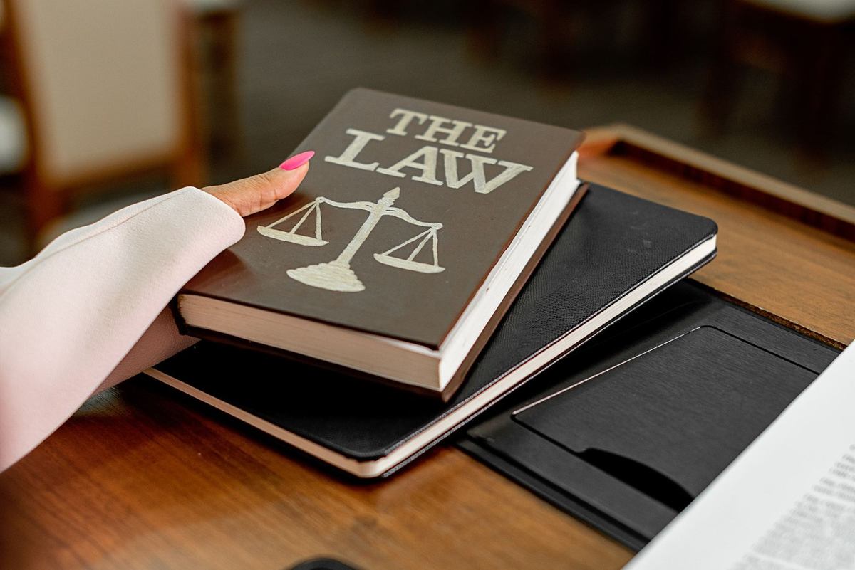 Livre noir "THE LAW" avec balance, main en blouse blanche, bureau en bois